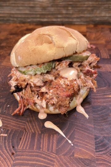 Honey Buffalo shredded rib sandwich with pickles and sauce on a wooden surface