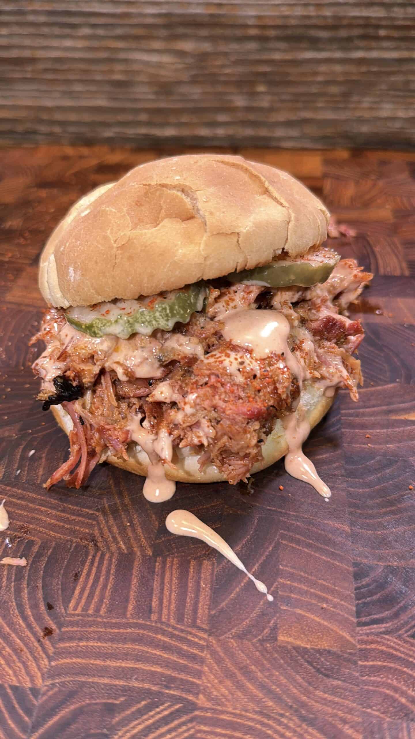Honey Buffalo shredded rib sandwich with pickles and sauce on a wooden surface