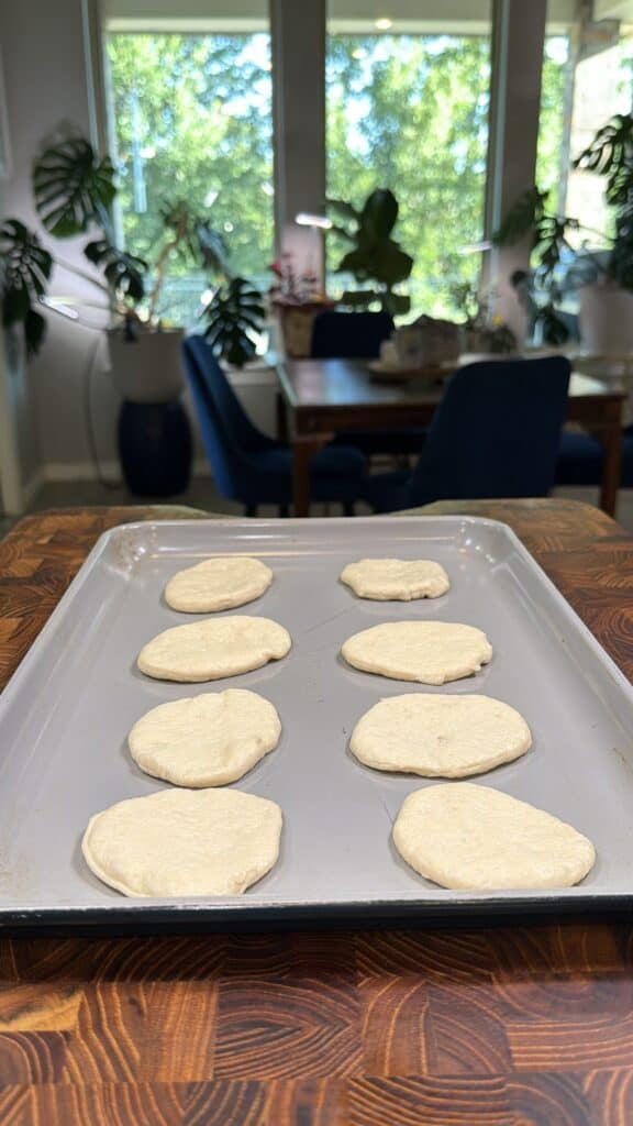 Eight unbaked mini pepperoni pizzas on a baking sheet.