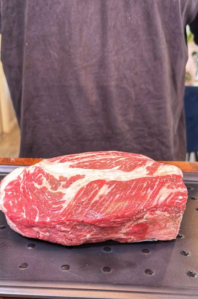 A raw chuck roast sits on a perforated tray.