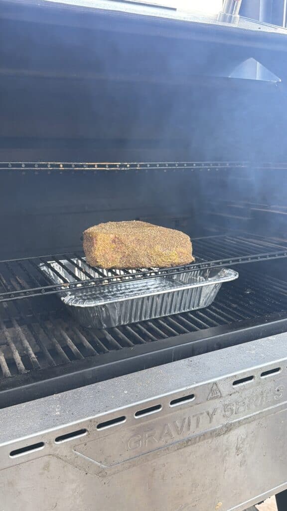 A seasoned chuck roast cooks on a smoker rack above a drip pan.