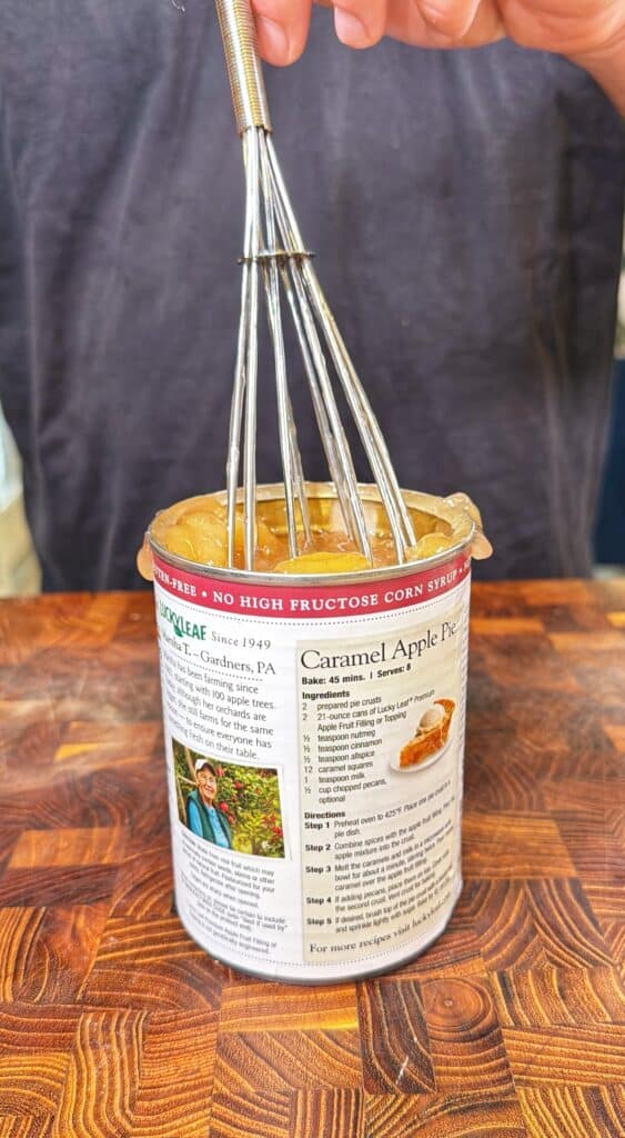 Mixing apple pie filling in an open can with a whisk