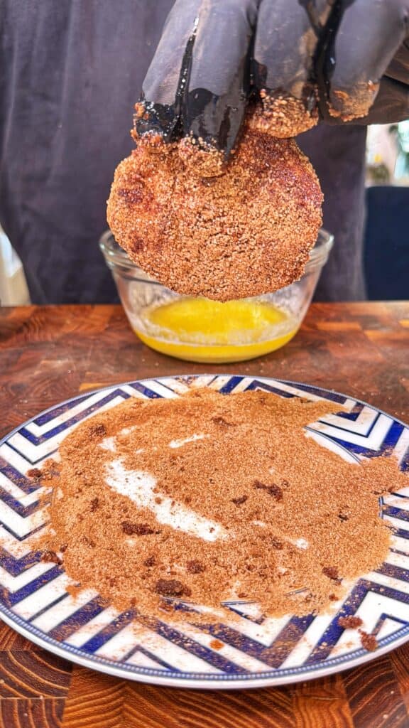 A biscuit half held over melted butter beside a plate of cinnamon sugar