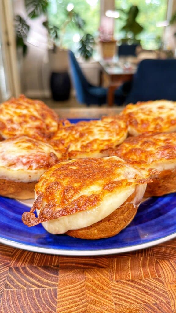 Six chicken Parmesan biscuit bites topped with melted golden-brown cheese sit on a blue plate.