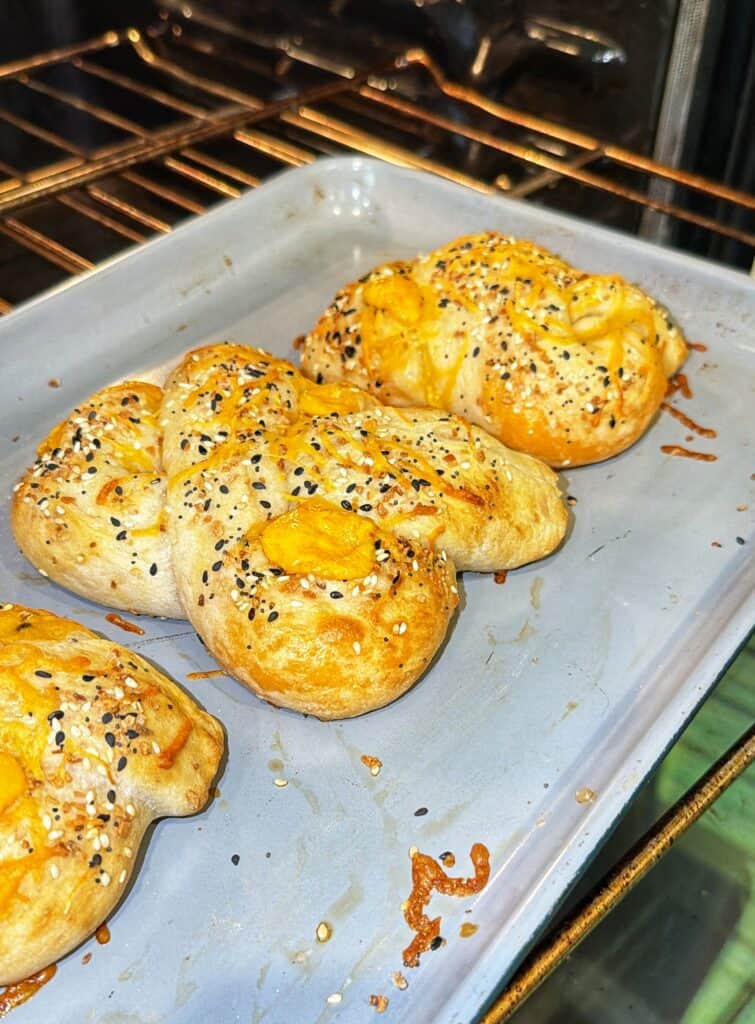 Four golden cheddar cheese stuffed pretzels bake on a tray in the oven.