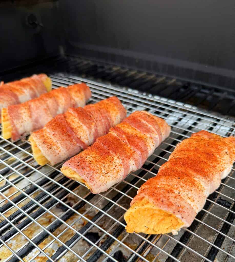 Seasoned bacon-wrapped Buffalo Chicken Shotgun Shells on a wire rack in a smoker.