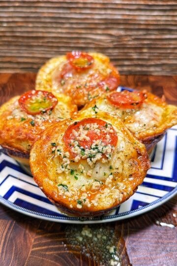 Four pepperoni pizza biscuit muffins topped with melted cheese, herbs, and garlic on a patterned plate.