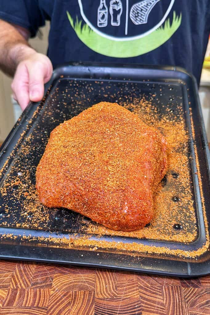 Raw turkey breast coated in a reddish-brown spice rub on a black tray.