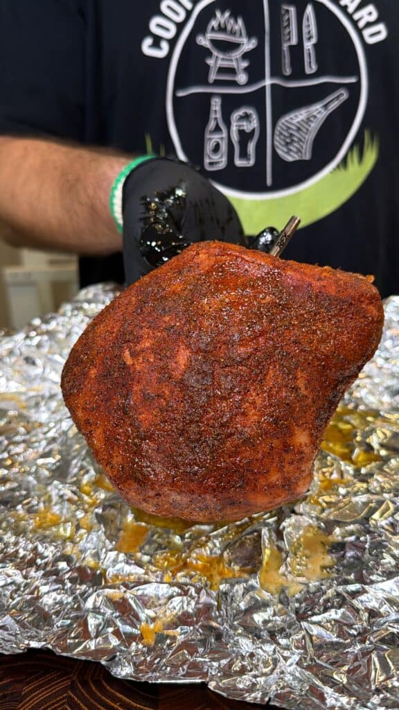 Gloved hand holding a seasoned turkey breast on foil.