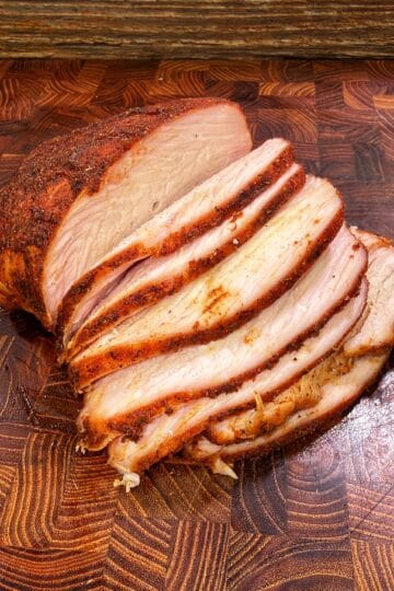 Sliced seasoned Cajun turkey breast on a wooden cutting board.