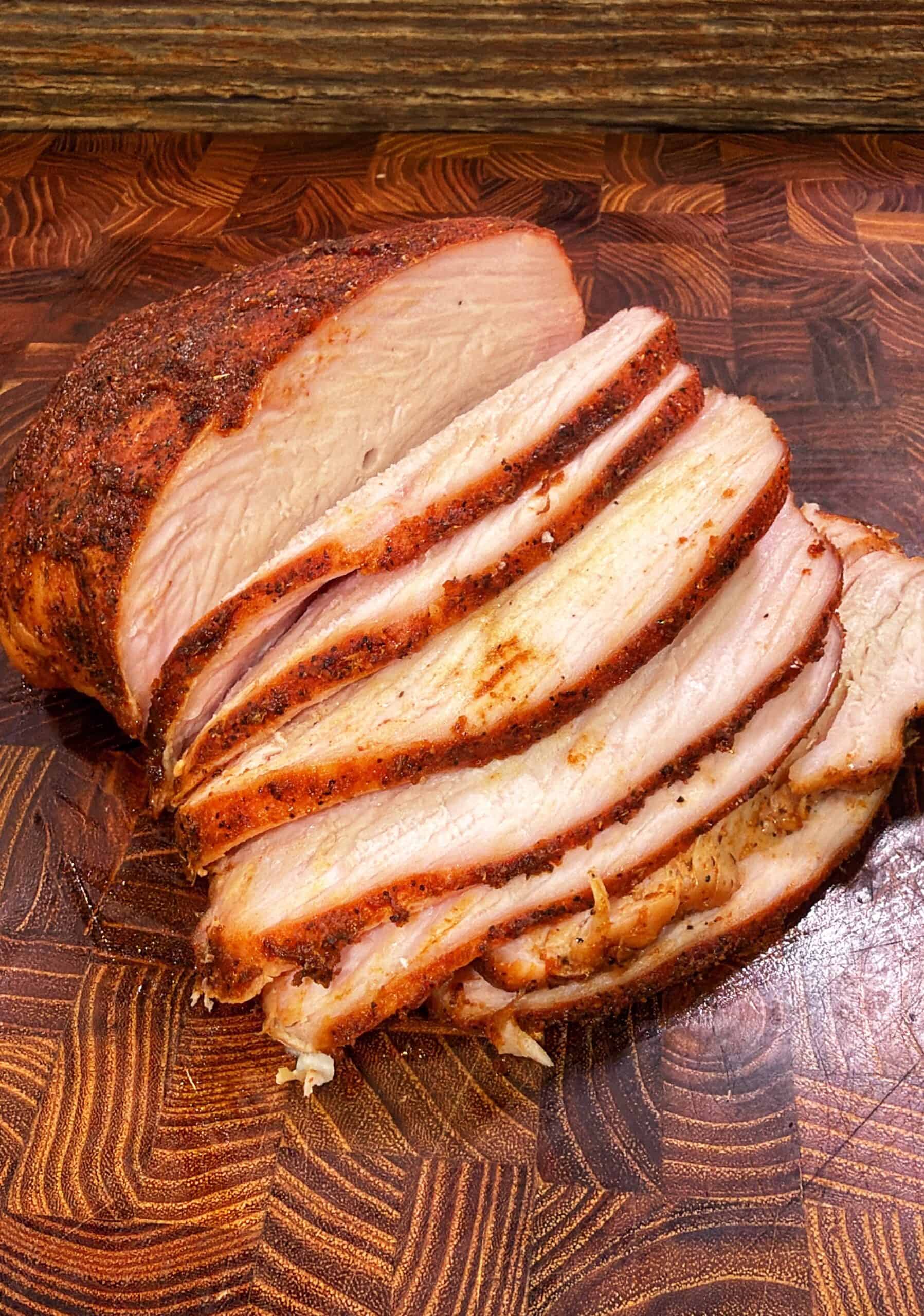 Sliced seasoned Cajun turkey breast on a wooden cutting board.