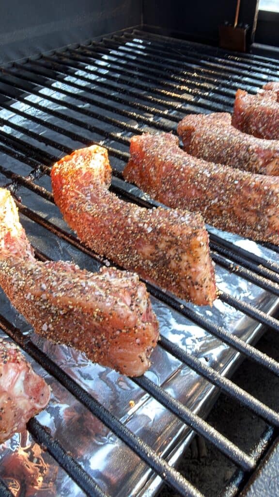 Seasoned party ribs cooking on smoker grates.