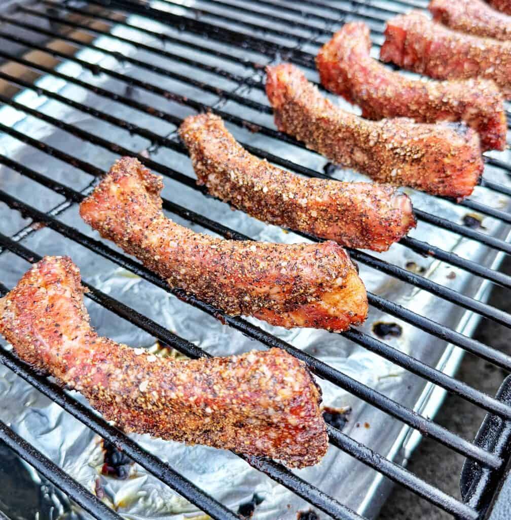 Seasoned party ribs cooking on smoker grates above a foil-lined tray.