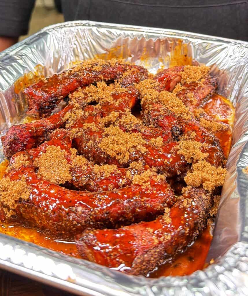An aluminum tray of party ribs topped with brown sugar.