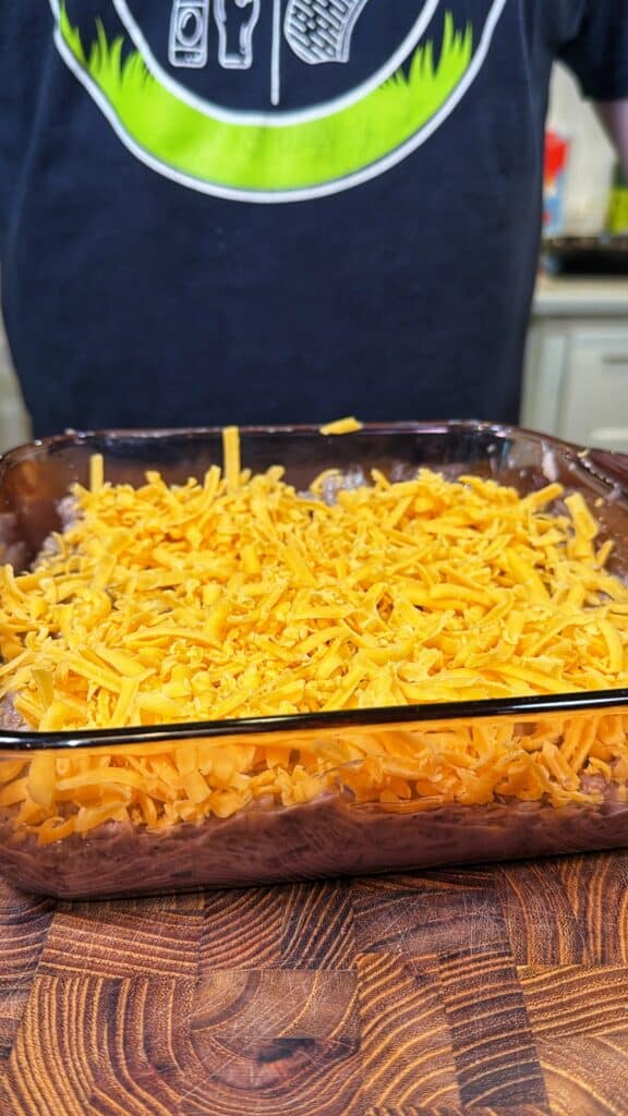 A glass baking dish of ground beef mixture topped with shredded cheddar cheese.
