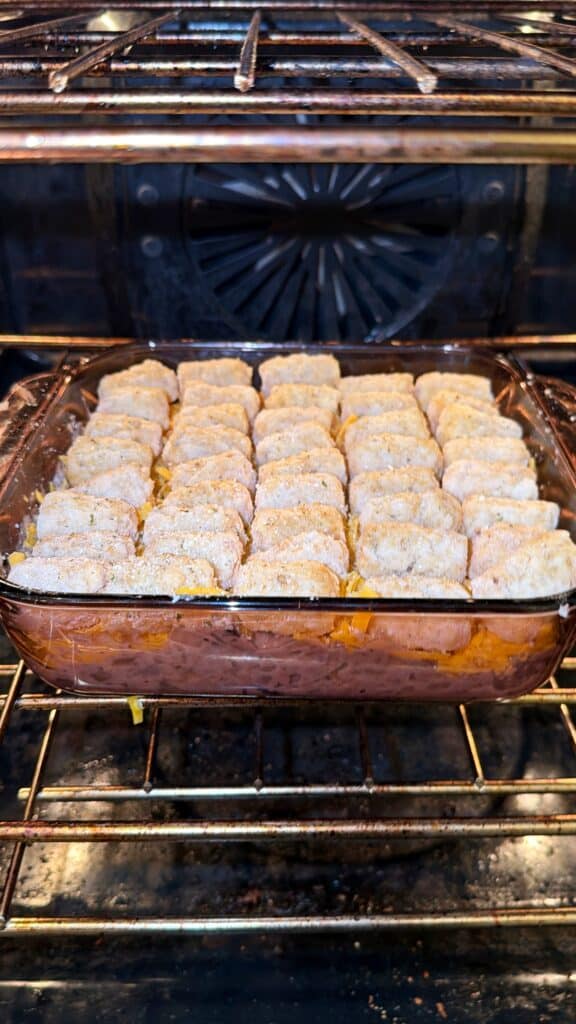 A glass casserole dish topped with a single layer of tater tots baking in an oven.