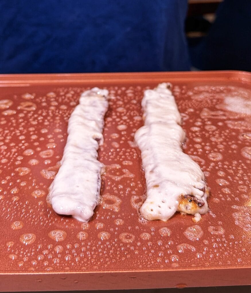Two pancake-battered bacon strips cooking on a griddle.