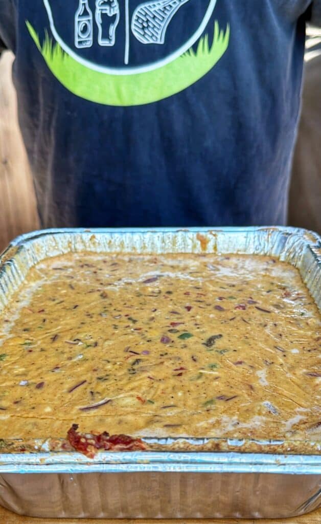 A foil tray of melted smoked cheeseburger queso with visible red onion.