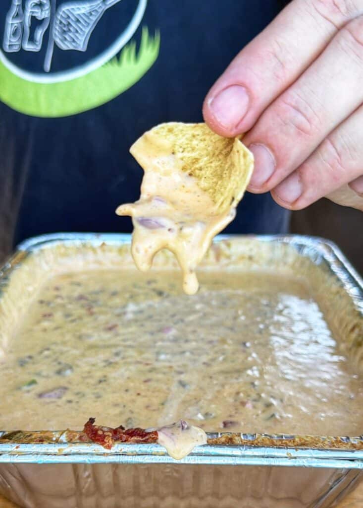 A tortilla chip dipped into creamy, chunky smoked cheeseburger queso.