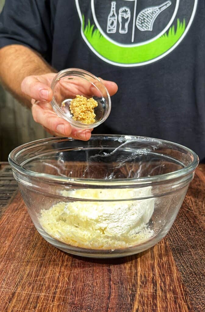 Minced garlic held over a glass bowl of cheese mixture.