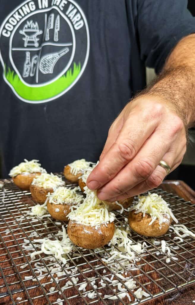 Cheese being added to mushroom caps on a wire rack.