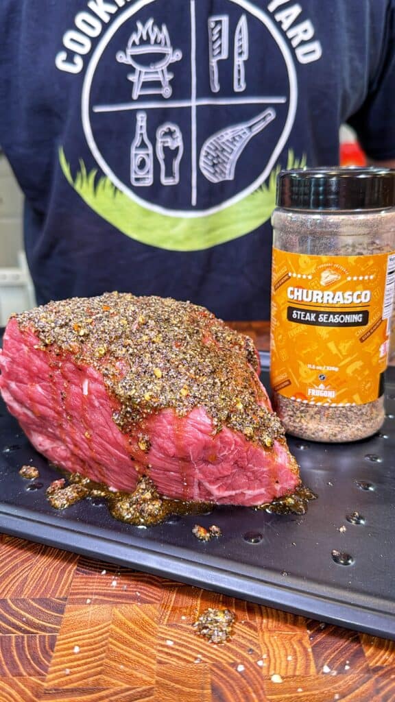 Raw beef roast covered in seasoning beside a jar of seasoning.