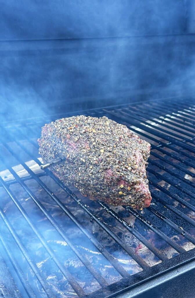 Seasoned beef roast smoking on a grill grate with a temperature probe inserted.