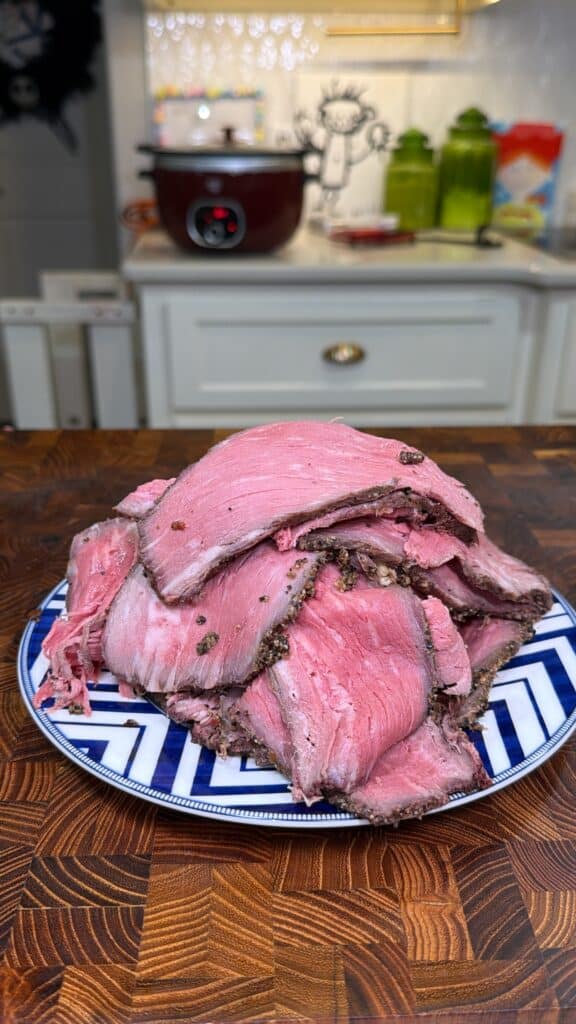 Pile of thinly sliced homemade deli-style roast beef on a patterned plate.