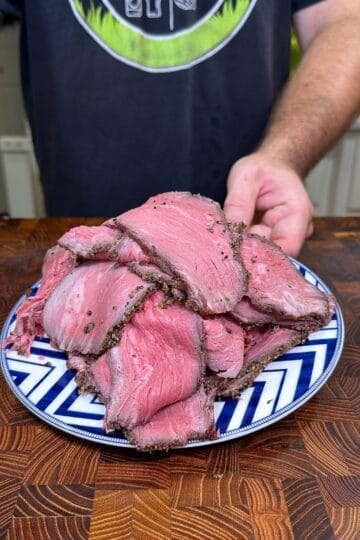 Plate piled with slices of homemade deli-style roast beef on a wooden cutting board.