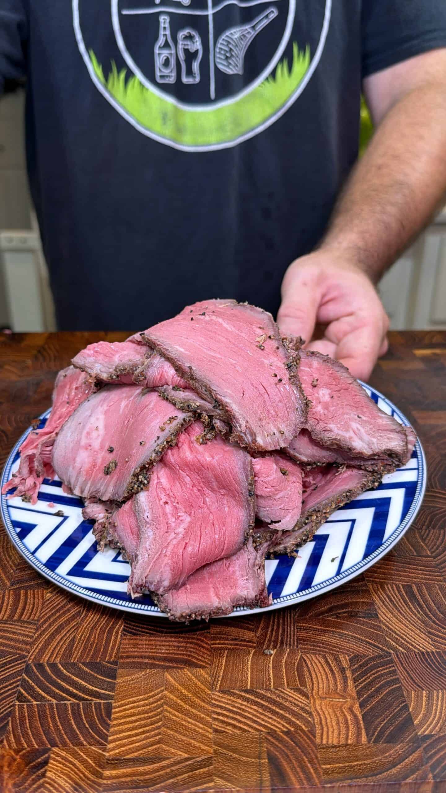 Plate piled with slices of homemade deli-style roast beef on a wooden cutting board.