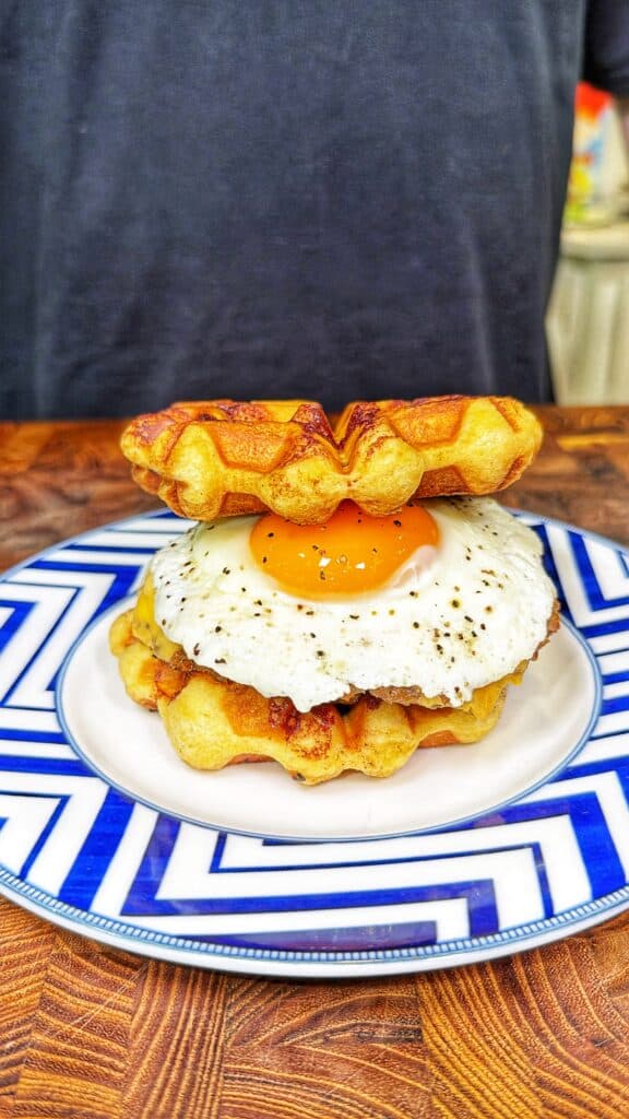 A cinnamon roll waffle sandwich with a fried egg between two waffles on a patterned plate.