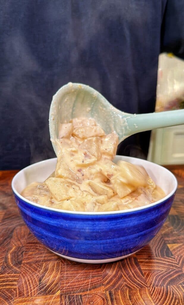 A ladle lifts steaming loaded potato soup from a blue ceramic bowl.