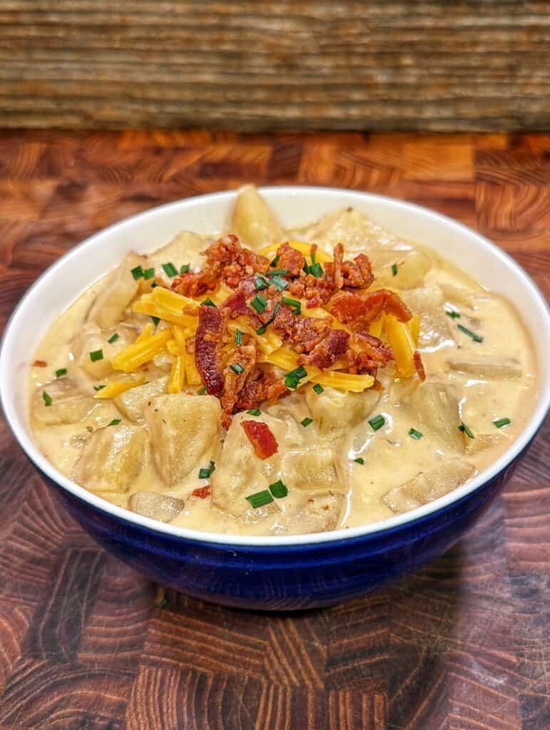 A bowl of slow cooker potato soup topped with shredded cheddar cheese, crumbled bacon, and sliced green onions.