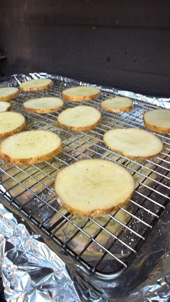 Potato slices arranged on a wire rack over a foil-lined baking sheet.