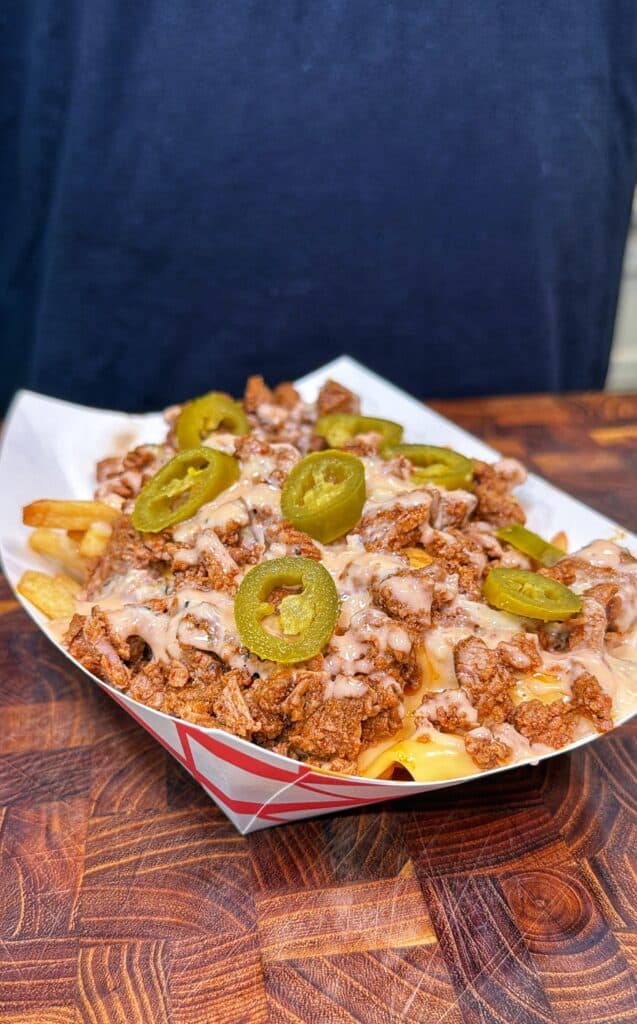 A paper tray filled with Cajun steak fries topped with steak, queso, and sliced jalapeños.