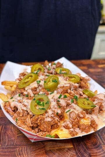 Cajun steak fries topped with steak, queso, spicy ranch, sliced jalapeños, and chives in a paper tray.