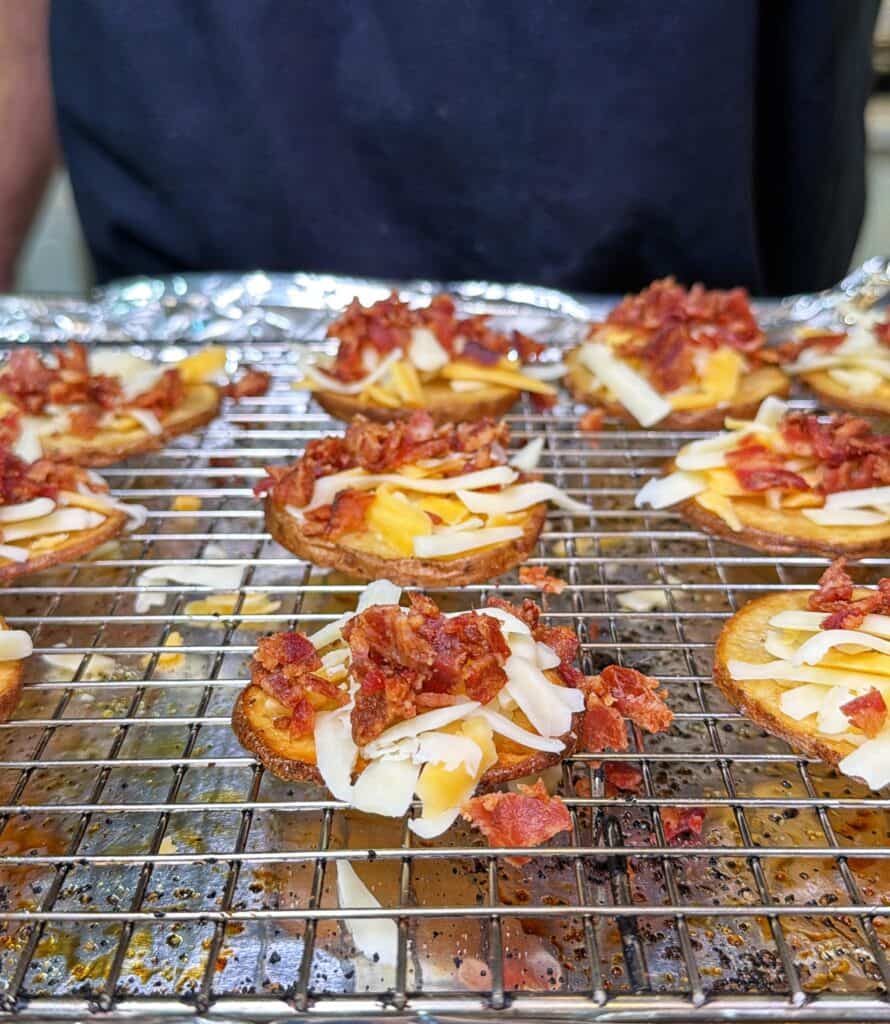 Potato nachos topped with shredded cheese and bacon on a wire rack.