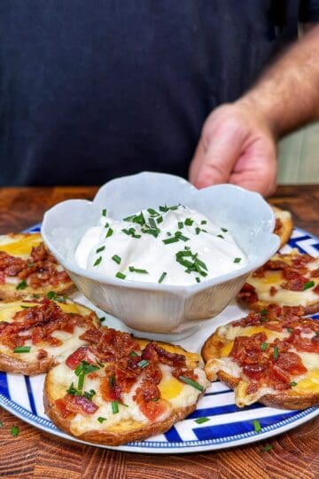 Potato pub nachos topped with melted cheese, bacon, and green onions, served with sour cream on a patterned plate.
