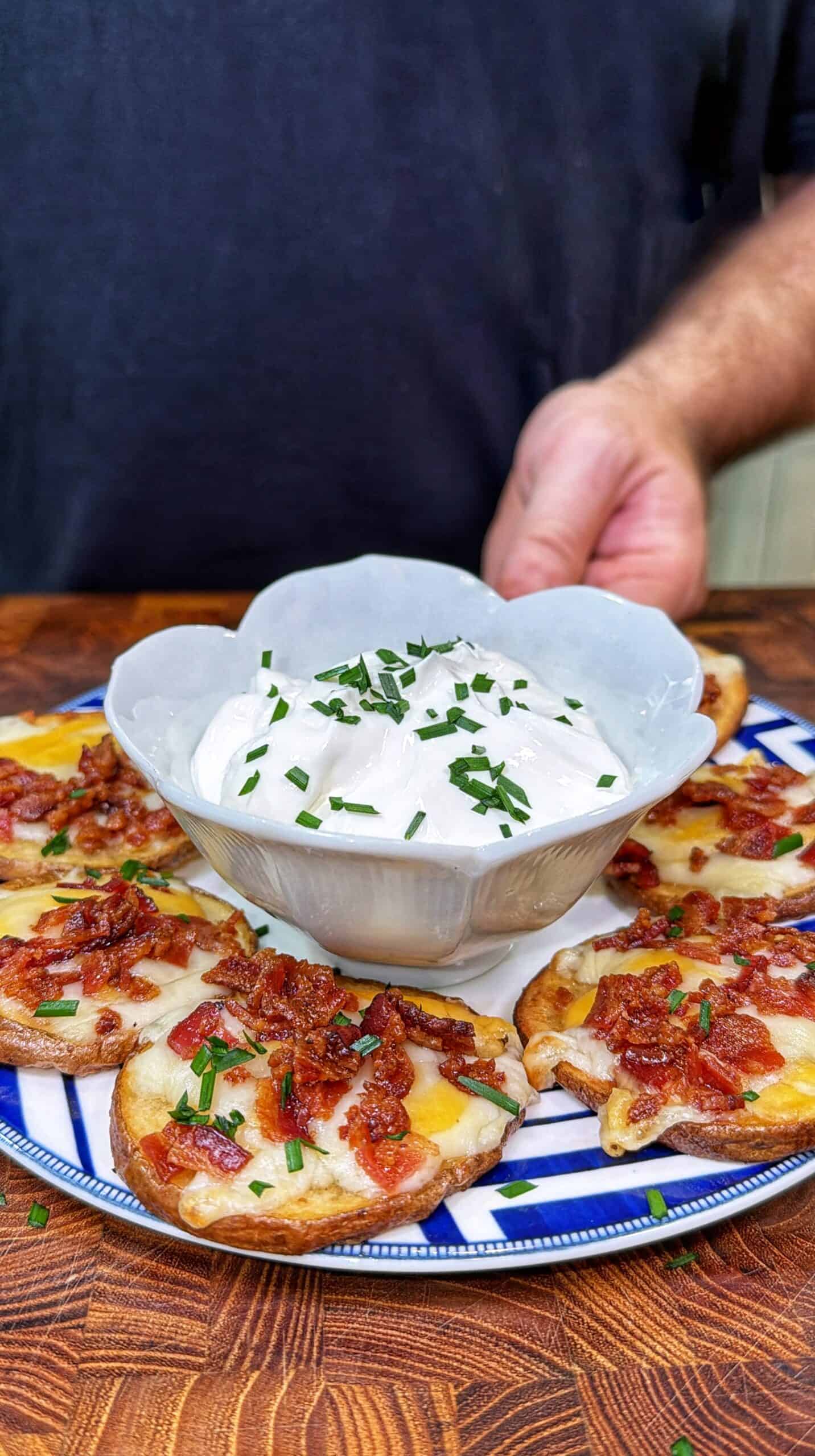 Potato pub nachos topped with melted cheese, bacon, and green onions, served with sour cream on a patterned plate.